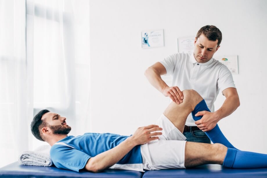 Physiotherapist massaging leg of football player lying on massage table in hospital
