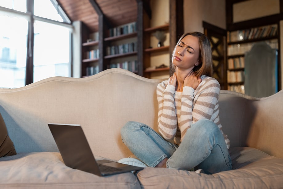 tired-woman-sitting-on-couch-with-pc-massaging-neck