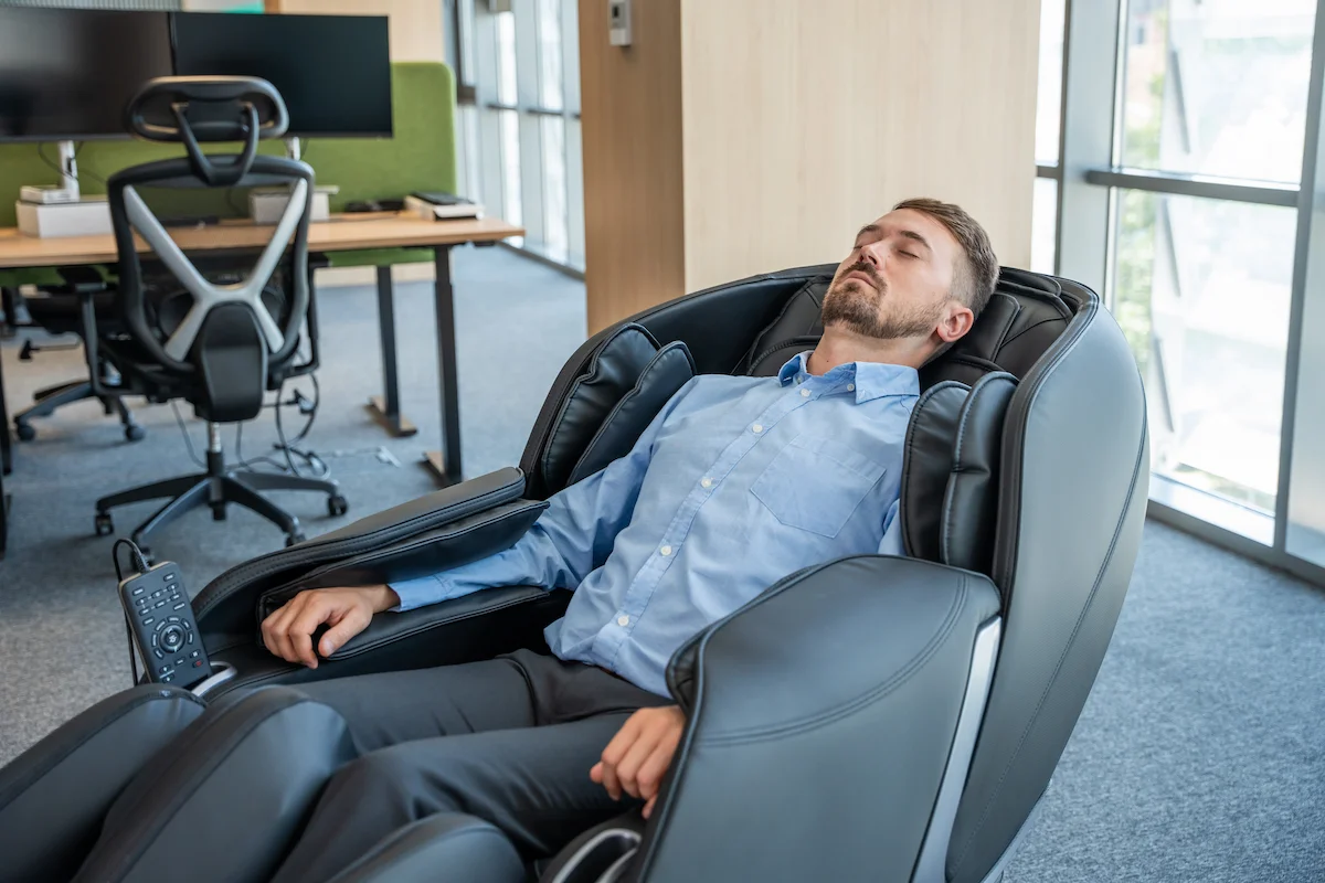 Barbat care se relaxeaza in pauza, la birou, intr-un scaun cu masaj Komoder Corporate